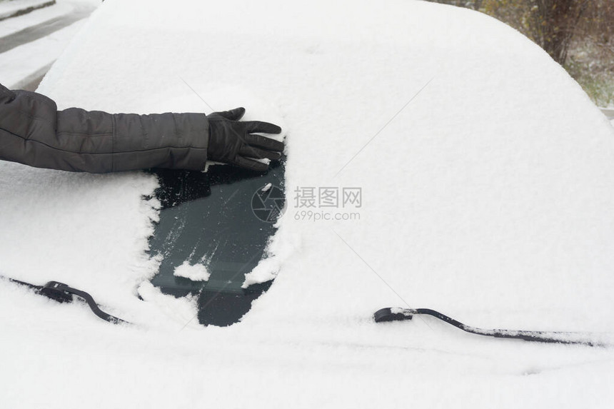 女人用手戴套从雪中清洗汽车积雪的汽车挡风玻璃冬季下雪期间停放的图片