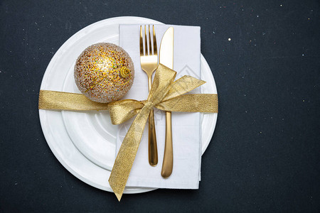 圣诞餐桌设置金餐具和白色盘子黑色背景图片