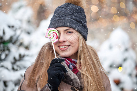 穿着冬衣微笑的年轻女子在圣诞雪街吃着多彩的棒糖图片