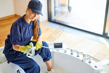 穿着蓝色工作制服洗浴戴保护黄色手套和帽子的女子图片