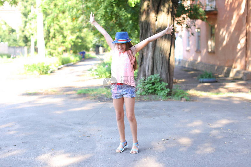 相当可爱的女孩在街头夏日在院子里跳跃有趣鬼混和大笑女孩身着粉色衬衫印花短裤深蓝色帽檐和蓝色图片
