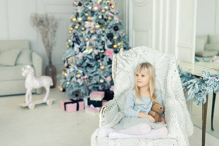 可爱的小女孩坐在圣诞树旁的椅子上图片