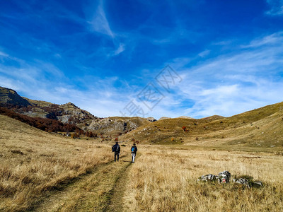 两个人在一条路上行走在一片空旷的草地中间被自然环绕在孤立的山区图片