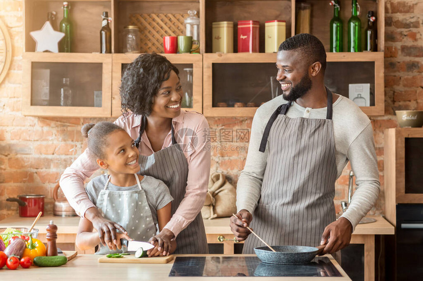 微笑的非洲母亲教小女儿切菜喜悦的父亲煎饭厨房图片