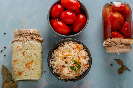 碗中的自制酸菜和咸西红柿以及浅蓝色背景的玻璃罐图片