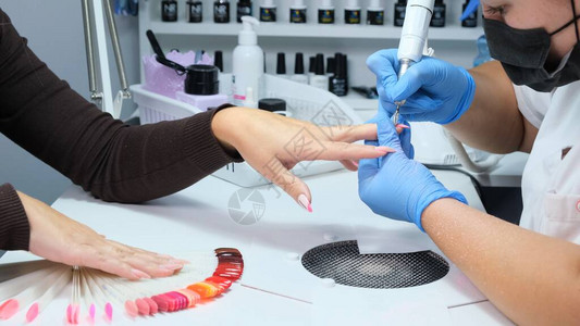 特写美甲沙龙的电动指甲钻在美容院进行硬件修指甲女美甲师从客户指甲上去除旧凝胶吸风格栅在美容院的指背景图片