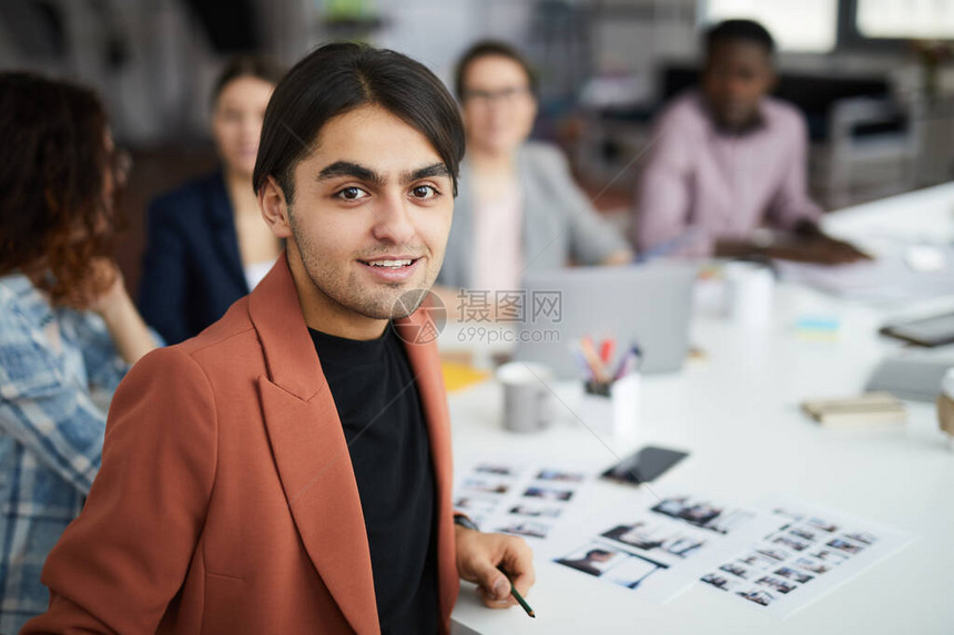 带着微笑的中东男人在与创造团队一起坐在会议桌边时看着照相机和复图片