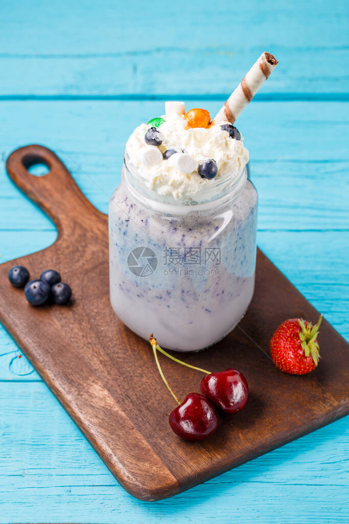 新鲜蓝莓奶昔和浆果放在蓝色桌子上的木桌边图片