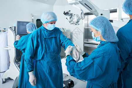 助理帮助外科医生在手术室站立图片