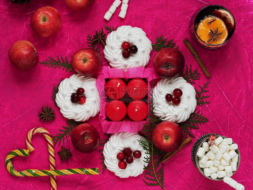圣诞静物与用喙苹果肉桂和蜡烛装饰的蛋白甜饼一杯热可加棉花糖和一杯酒紫红色背景上的图片
