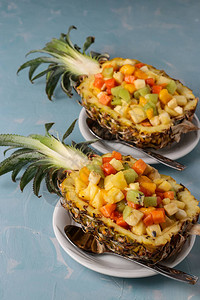 浅蓝色背景的白盘上菠萝半份热带水果沙拉图片