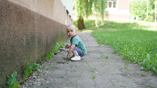 独自穿着绿色T恤的小男孩在房子前面的草坪上石膏墙壁附近图片