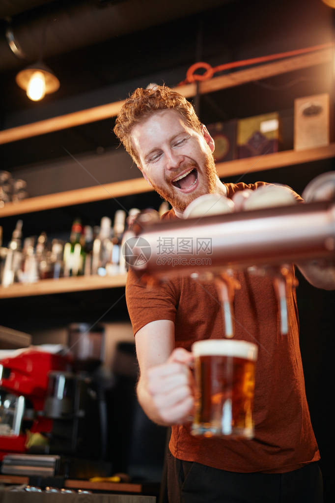 英俊的caucasian酒吧男招待站在酒吧里喝啤酒图片