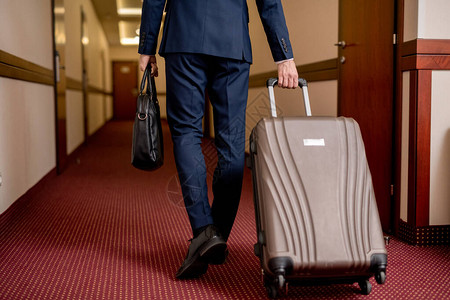 离开酒店时带着手提箱和手提包沿着走廊移动的优雅商人图片