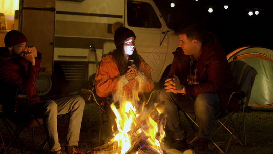 女孩在秋天寒冷的夜晚向营地火灾周围的朋友讲述一个可怕的故事Retro露营车背景图片