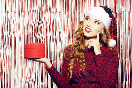 戴着明亮圣诞帽的漂亮女孩拿着一个红色的盒子图片