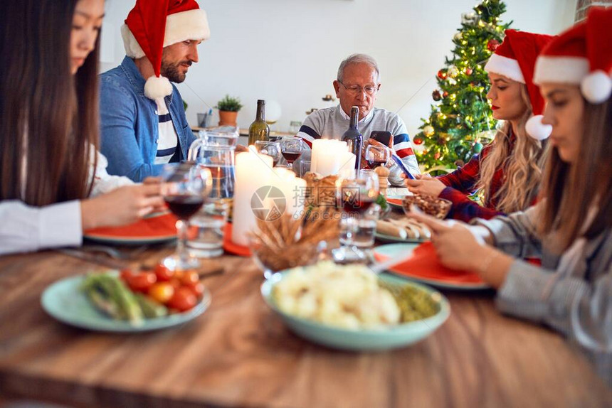 美丽的家庭戴着圣诞老人的帽子微笑快乐和自信在家用智能手机吃烤火图片