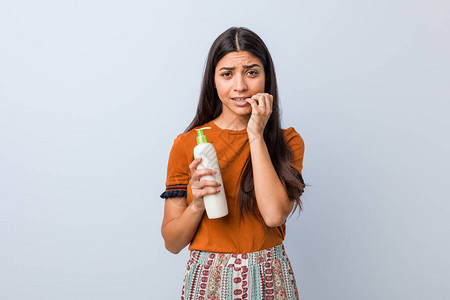 年轻阿拉伯女人拿着奶油瓶咬指甲紧张和非图片
