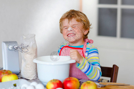 可爱的小快乐金发学龄前儿童男孩在国内厨房烤苹果蛋糕和松饼图片