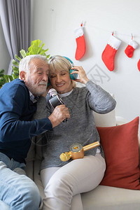 老年人和妇女在装饰着圣诞树的客厅里快乐地唱歌和用耳机一起听图片