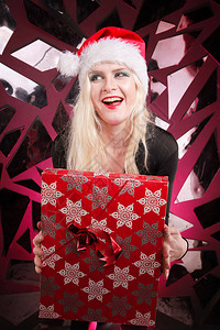 快乐可爱苗条的年轻女子在圣诞毛皮帽子拿着礼品盒在黑暗的夜总会坏顽皮的图片