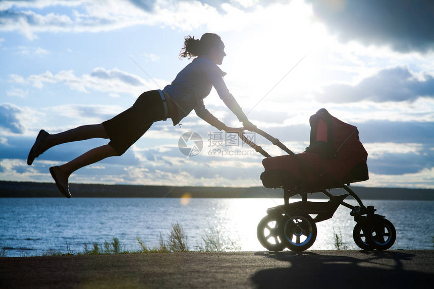 日落时一个年轻母亲在婴儿行车里为婴图片