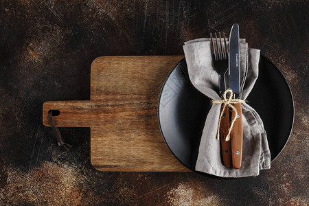 深棕色背景板上的餐具亚麻餐巾和木制服务板上带木柄图片