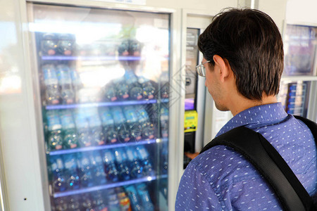 年轻男背包客旅游者在自动售货机上选择零食或饮料图片