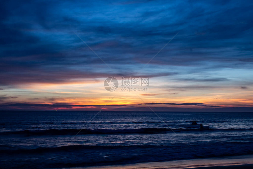 卡伦海滩的蓝色阴影日落太阳正落在海洋上空天空中的黑暗是蓝色的阴影在光滑的云层中混合着橙色图片