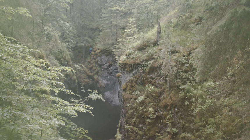 洞穴和旅行者在森林中的视图影视素材远处的旅行者站在绿色森林岩石中的黑色洞穴上有神秘峡谷和黑图片