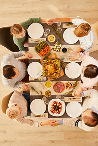 家庭坐在餐桌上举手祈祷在庆祝感恩节的饭前的高角度视角图片