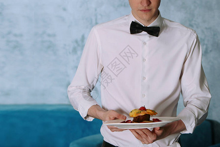 一位年轻的男服务员手里拿着一份餐厅菜单上的熟菜餐厅业务的概念照片没图片