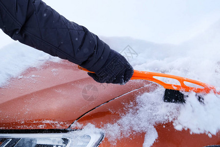 白雪皑刷在男人手中男人从雪中清除橙色汽车汽车被雪覆盖汽车司图片