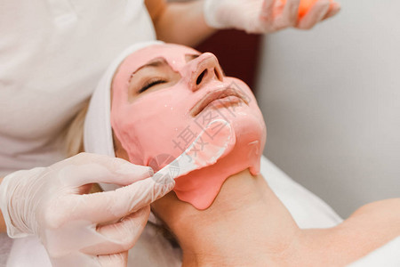 医生美容师在女脸上涂抹抗衰老面膜女孩躺在美容程序图片