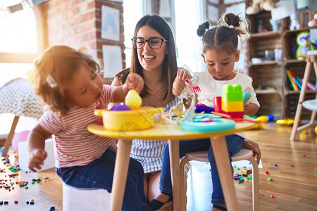 年轻漂亮的老师和幼儿在幼儿园用塑料食品和图片