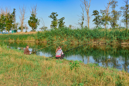 一男女坐在河岸边捕鱼钓图片