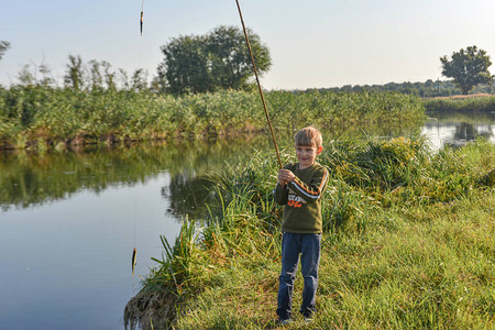 一个喜悦和快乐的男孩为第一次在河边钓鱼杆上捕获图片