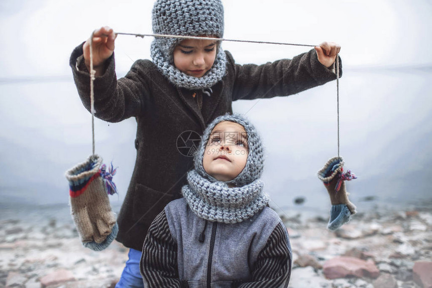 戴着针织灰色帽子的漂亮小女孩提议在冬天的降雪寒冷的天气户外的生活方式肖像中与她冻僵的弟图片