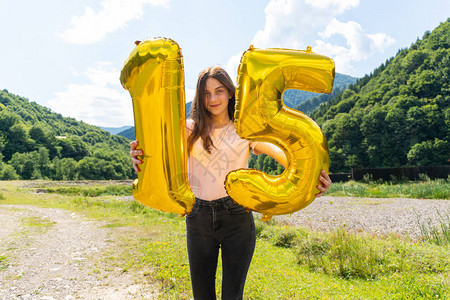 年轻女孩拿着15号金色气球在户外庆祝生图片