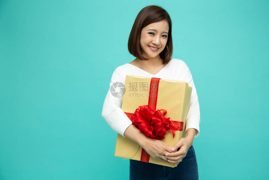 快乐美丽的亚洲女人微笑着与浅绿色背景上孤立的金色礼品盒图片