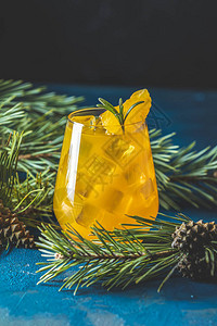 深蓝色混凝土背景的玻璃杯中加入橘子和迷迭香的黄橙鸡尾酒图片