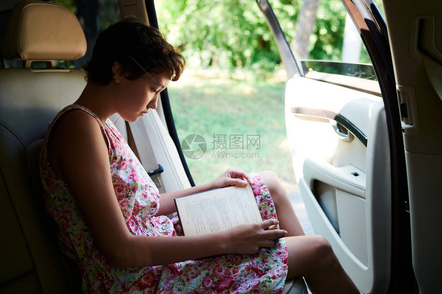 在开车时热情地阅读书的春前少女侧面观景图片