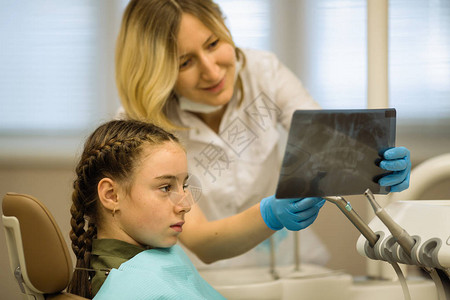 牙医妇女对坐在牙科诊所牙科诊疗椅上的一位小女病人进行X光图片