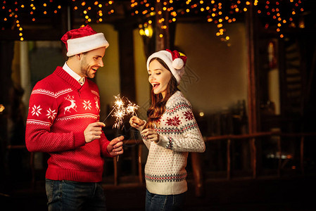 快乐的一对年轻夫妇在圣塔帽子和温暖毛衣盛装火花背景图片