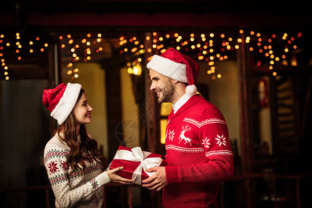 穿着温暖毛衣和圣塔帽子的年轻快乐情侣拿着礼物盒图片