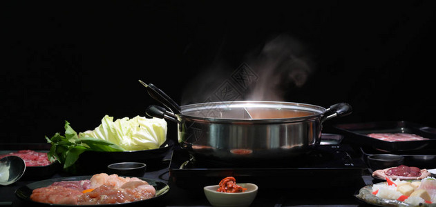 火锅涮锅鲜肉片海鲜和黑色背景蔬菜图片