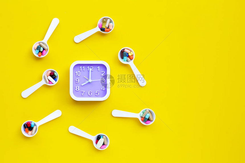 时钟与五颜六色的片剂与胶囊和药丸在黄色背景图片