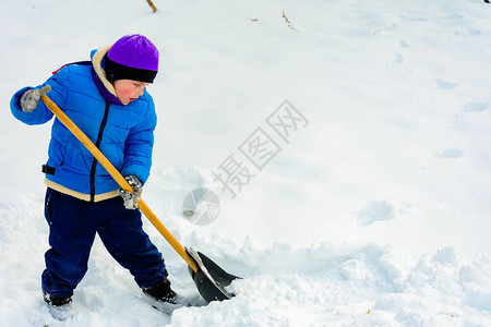 微笑的男孩在铲子上背着雪图片