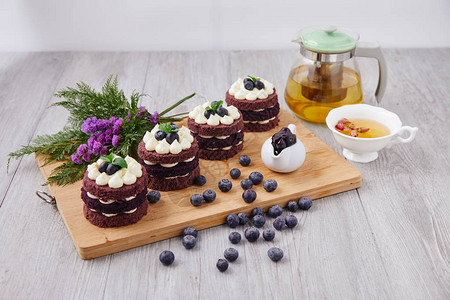 四条棕色蛋糕上面有蓝色的白莓夹在一起把花茶壶和浆果作为装饰图片