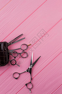 粉红色木制桌子上的发型剪刀专业理发师剪刀的顶端视图片